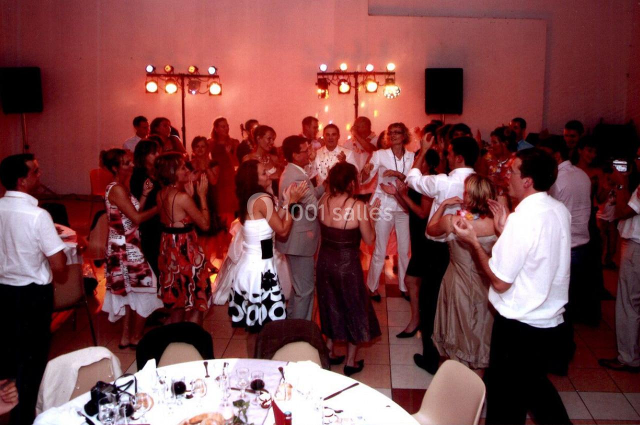 Des invités dansent et applaudissent lors d'une fête dans une salle éclairée par des lumières colorées.