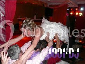 Une mariée en robe blanche est portée en l'air par des invités lors d'une fête avec éclairages colorés.