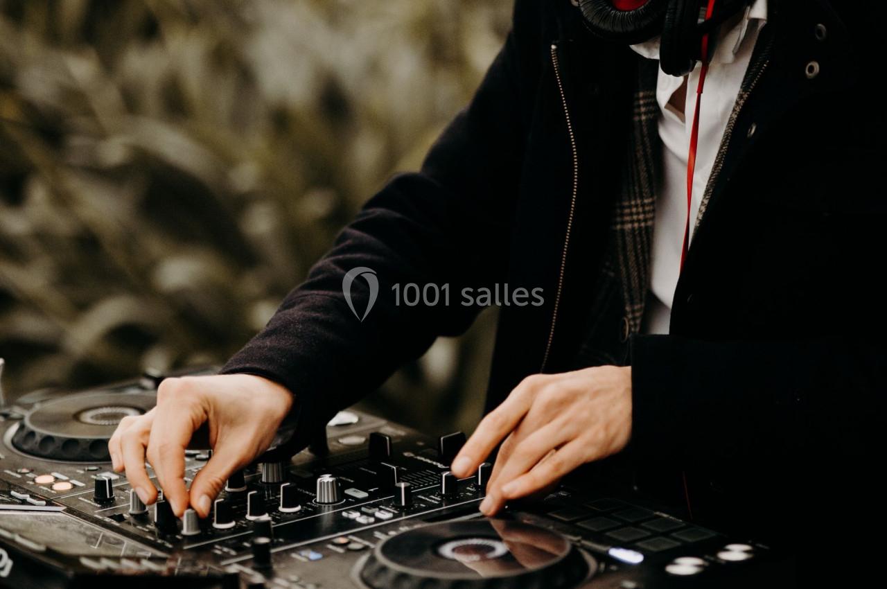 Un DJ portant un masque ajuste les commandes d'une table de mixage dans un environnement extérieur.