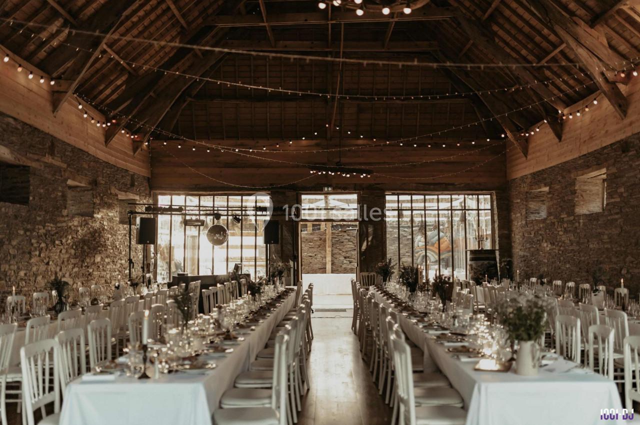 Grande salle en pierre avec tables dressées pour un banquet, éclairée par des guirlandes lumineuses suspendues.