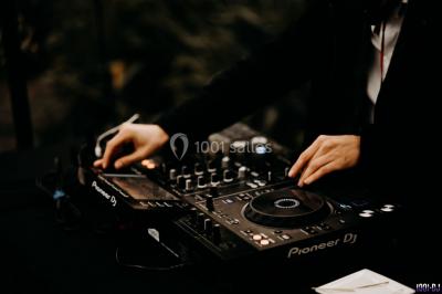 Homme souriant avec une moustache, portant une chemise sombre, devant un arrière-plan flou de verdure.