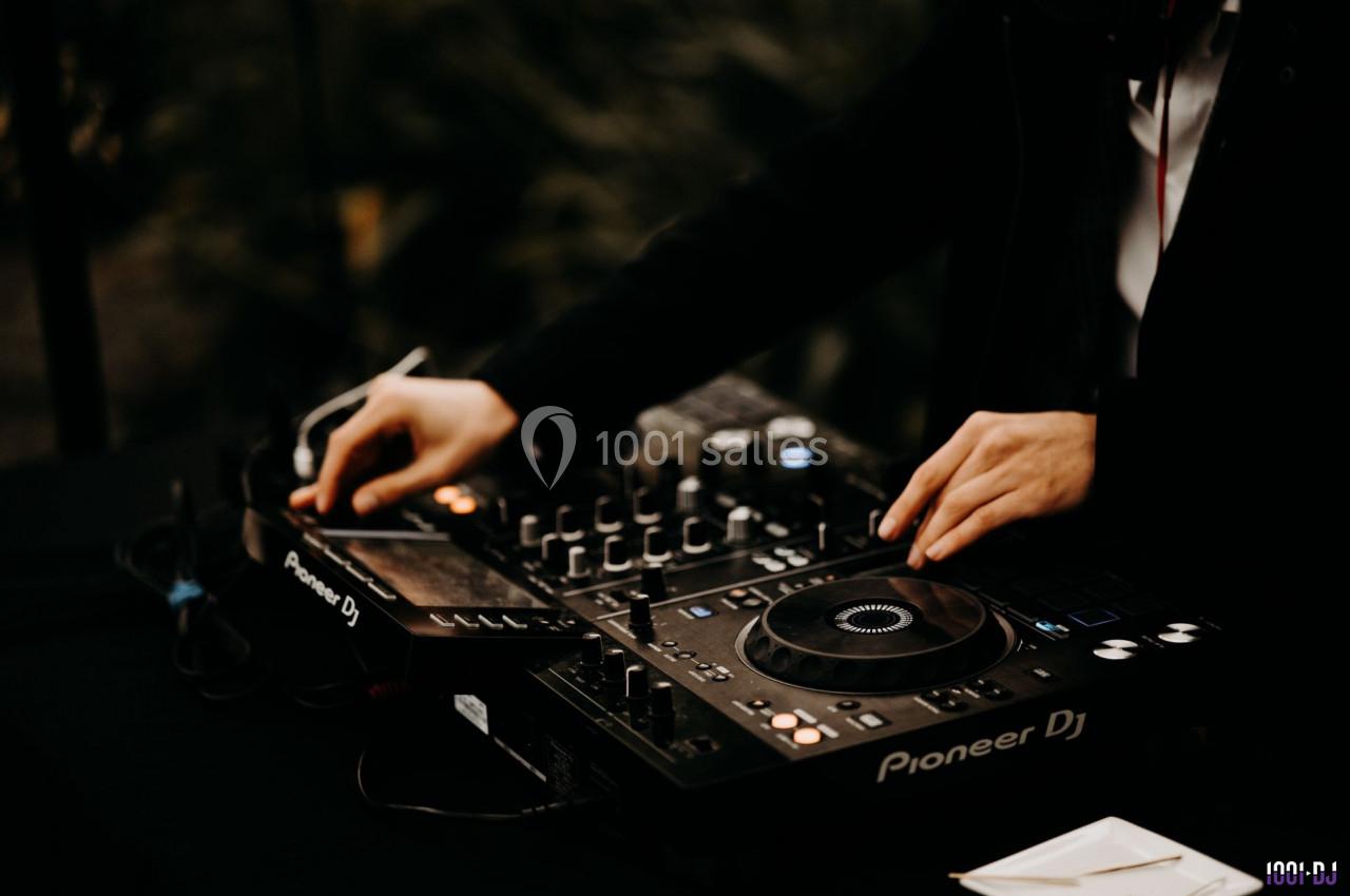 Un DJ manipule une table de mixage et des platines dans un environnement sombre.