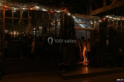 Homme souriant avec une moustache, portant une chemise sombre, devant un arrière-plan flou de verdure.