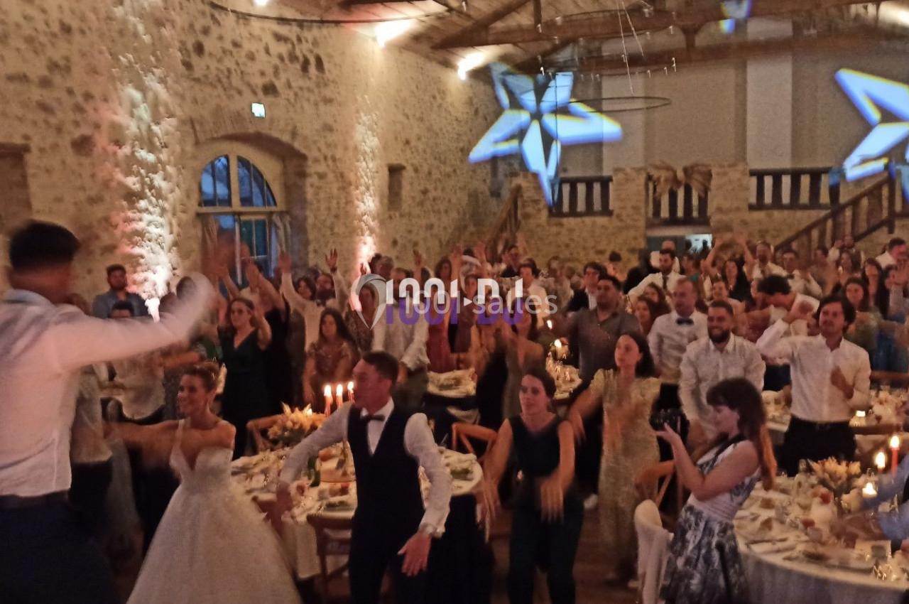Salle de réception en pierre avec invités dansant et décorations lumineuses en forme d'étoiles au plafond.