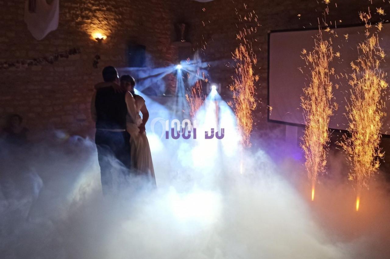 Un couple danse dans une salle sombre éclairée par des étincelles et des effets de fumée.