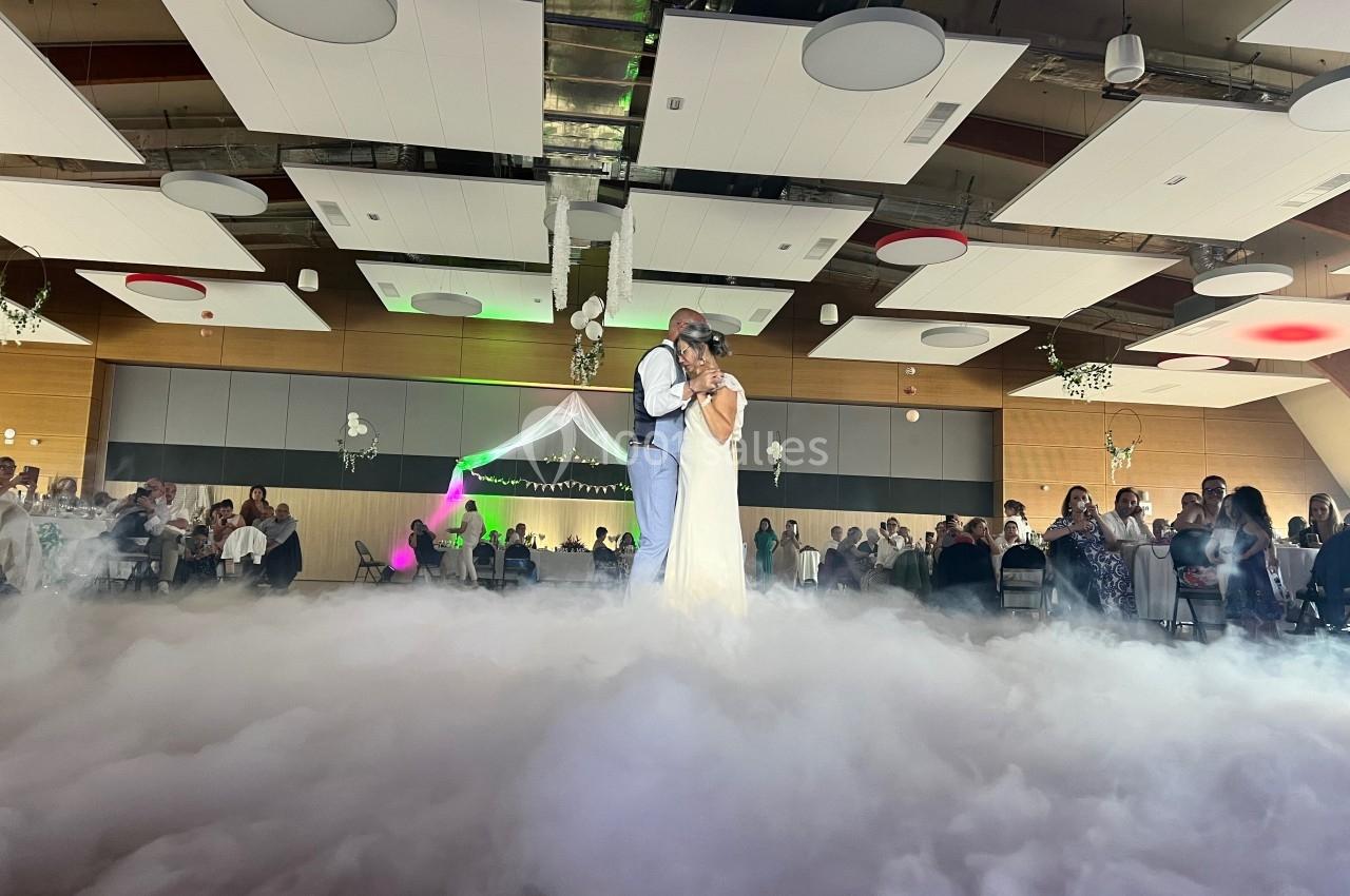 Un couple danse au milieu d'une piste enveloppée de fumée, entouré d'invités dans une salle décorée.