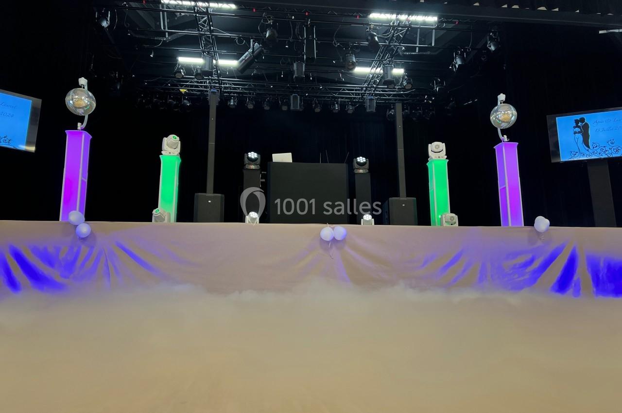 Scène décorée avec des colonnes lumineuses colorées, des boules disco et un fond de fumée sous un éclairage de spectacle.