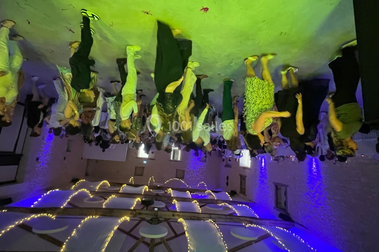 Des personnes dansent dans une salle éclairée par des lumières colorées, avec un plafond décoré de guirlandes lumineuses.