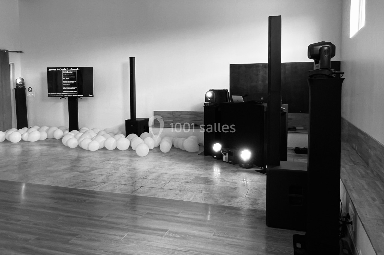 Salle de réception avec équipement audio, éclairage et ballons blancs dispersés au sol.