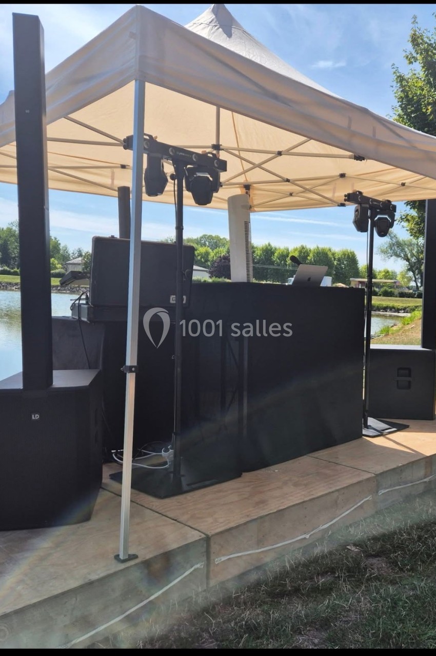 Équipement de sonorisation et éclairage installé sous une tente blanche près d'un plan d'eau.