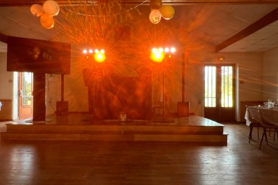 Salle de réception avec scène éclairée par des projecteurs orange, décorée de ballons suspendus.
