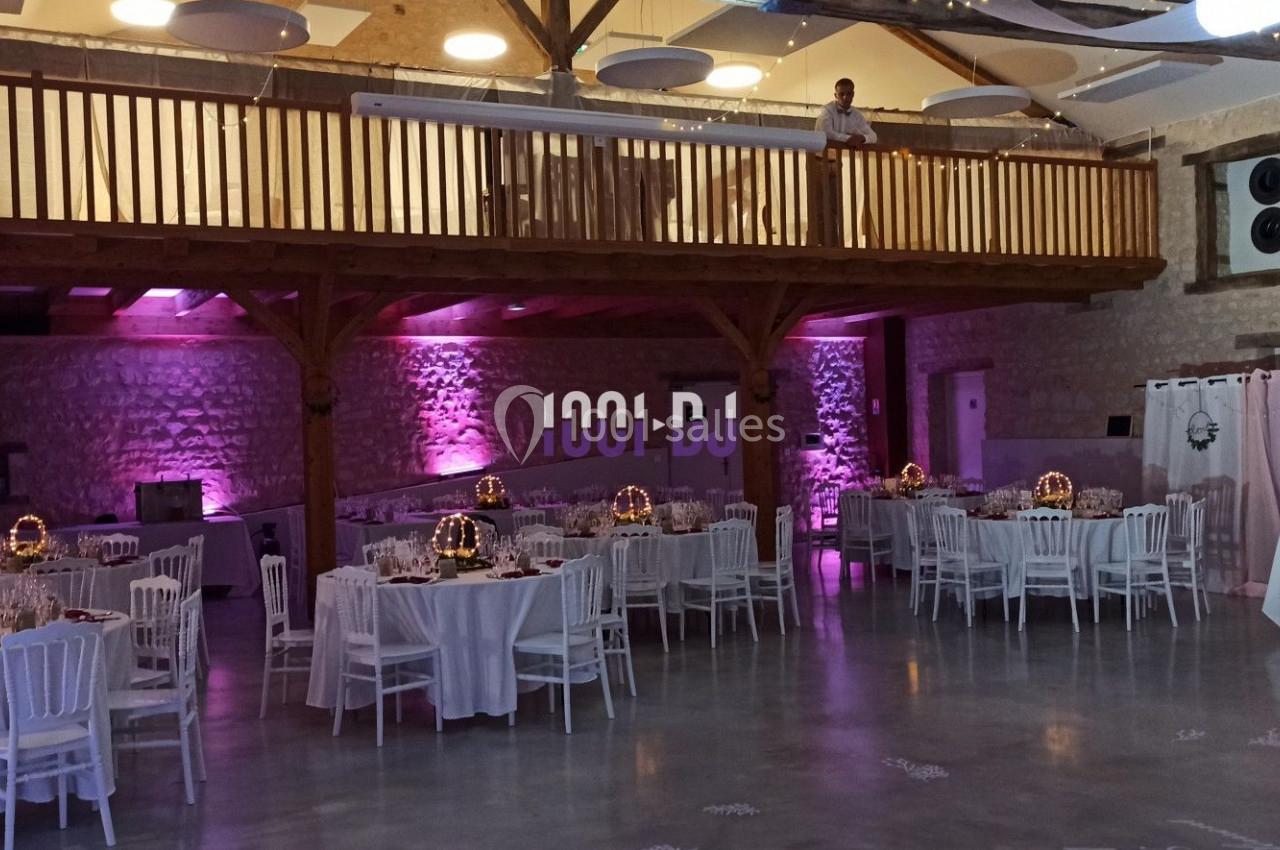 Salle de réception décorée avec des tables dressées, éclairage rose et mezzanine en bois.
