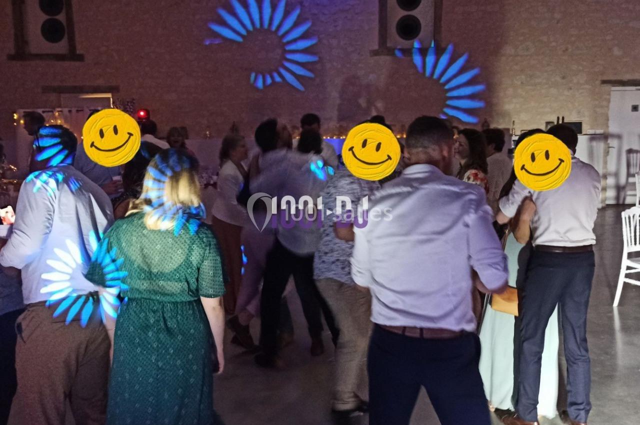 Des personnes dansent dans une salle éclairée par des lumières colorées, avec des tables dressées en arrière-plan.