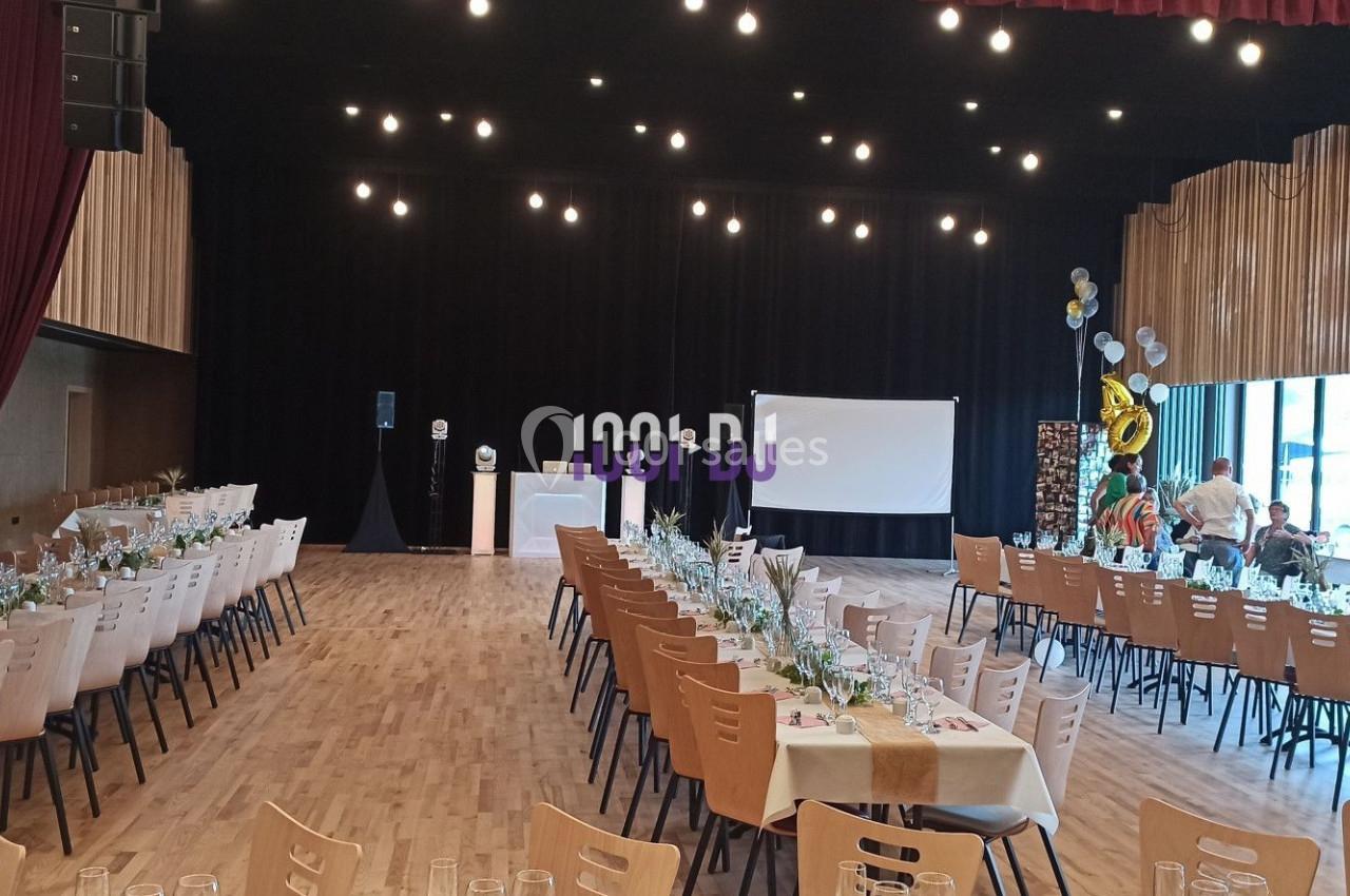 Salle de réception décorée avec des tables dressées, un écran de projection et des ballons en arrière-plan.