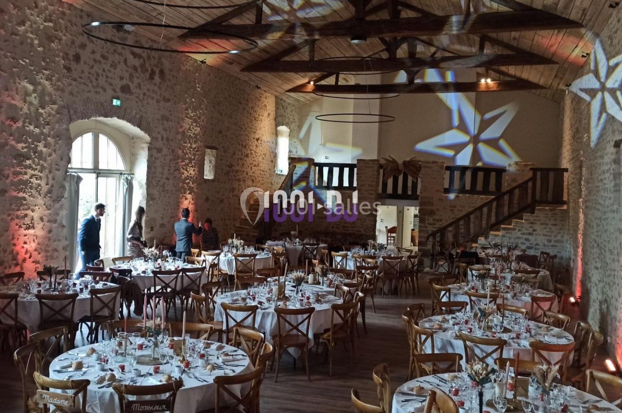 Salle de réception en pierre avec tables rondes dressées, éclairages décoratifs et mezzanine en bois.