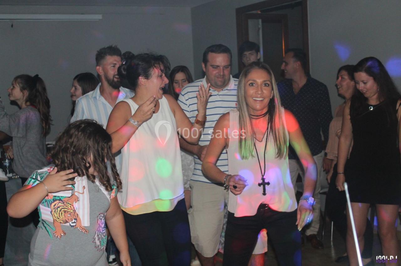 Des personnes dansent et s'amusent dans une salle éclairée par des lumières colorées lors d'une fête.