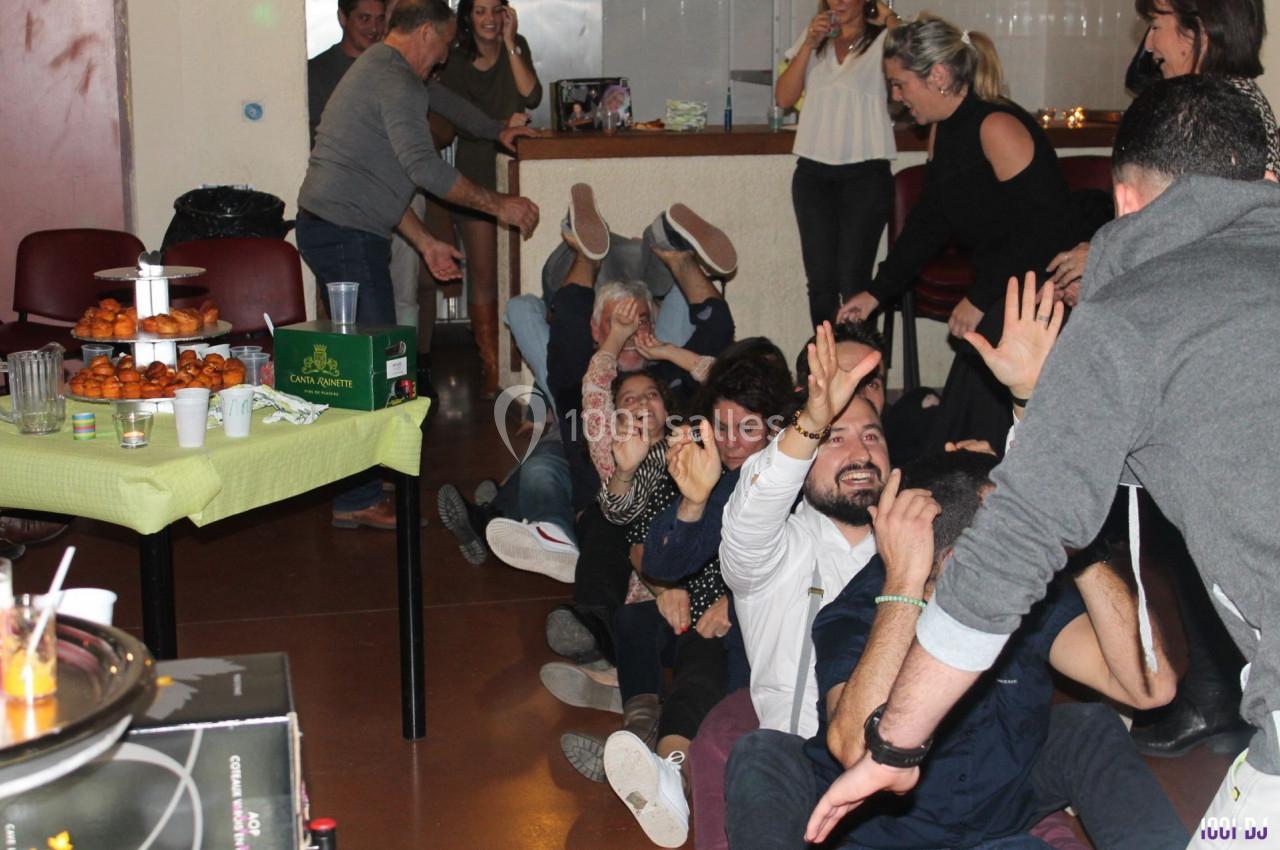 Des personnes assises au sol en file, participant à une activité ludique dans une salle conviviale avec des tables dressées.