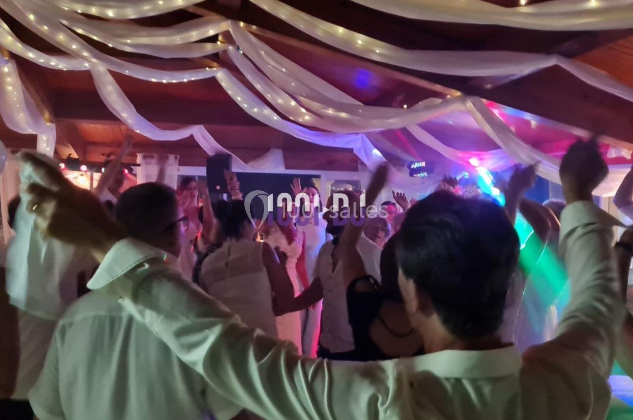 Des personnes dansent sous des décorations lumineuses et des drapés blancs dans une salle festive.