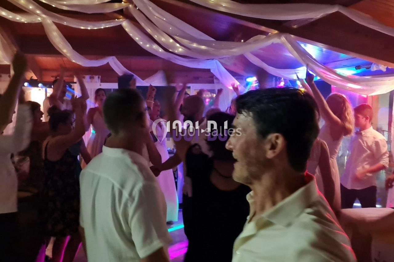 Groupe de personnes dansant dans une salle décorée avec des guirlandes lumineuses et un éclairage coloré.