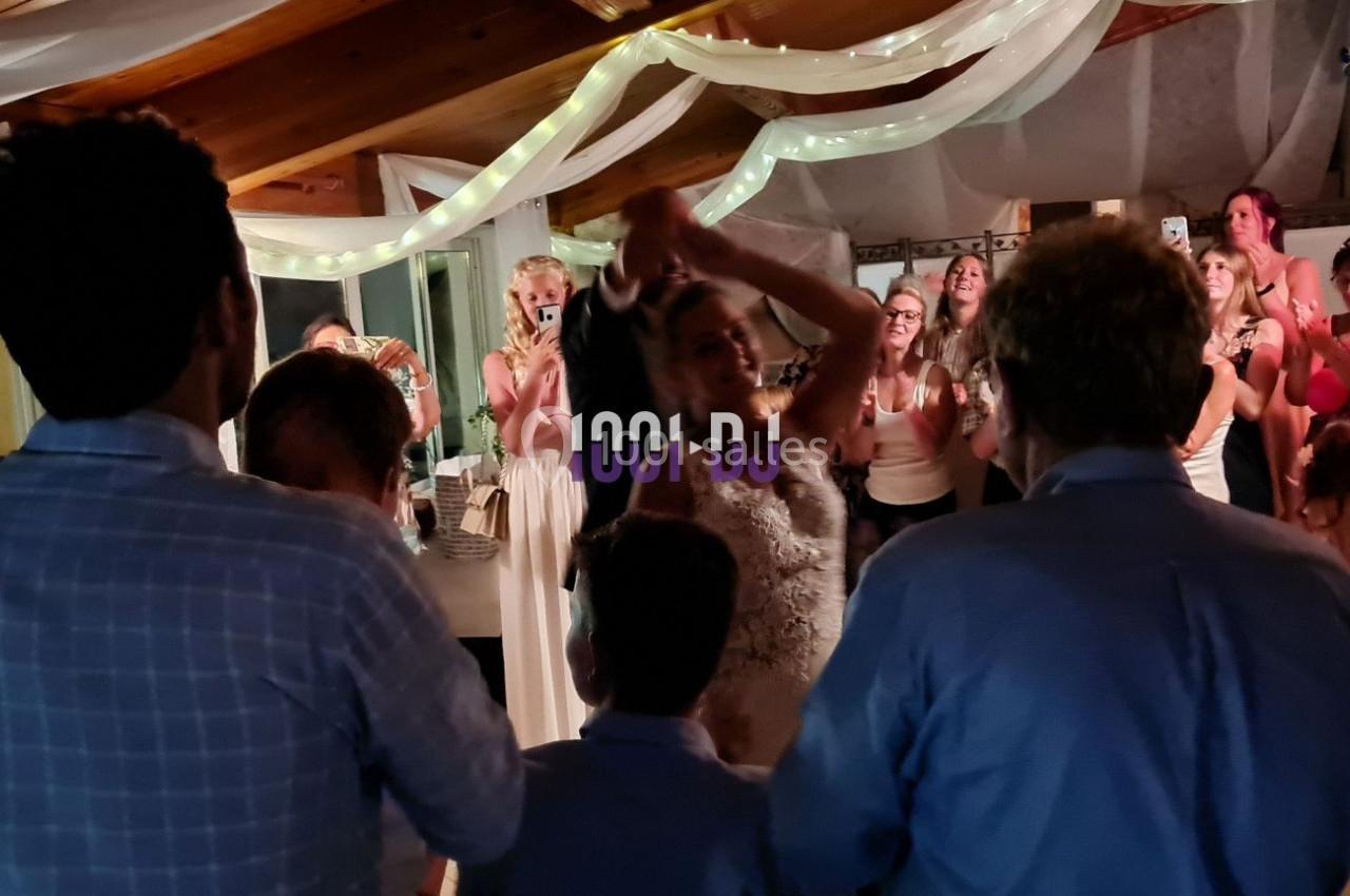 Des invités entourent une mariée dansant sous des lumières tamisées lors d'une réception festive en intérieur.