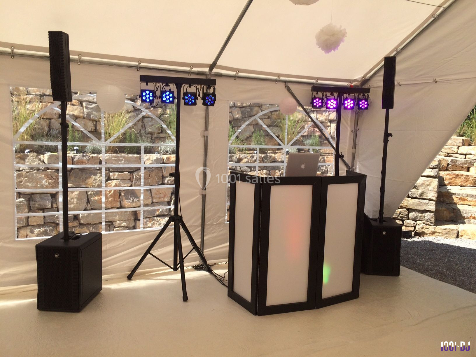 Équipement de sonorisation et éclairage installé sous une tente blanche avec un mur de pierres en arrière-plan.
