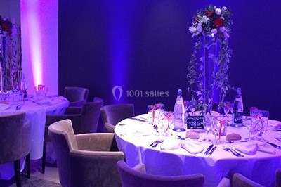 Salle de réception décorée avec des lumières violettes, tables dressées et écran affichant des prénoms.