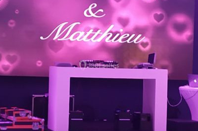 Salle de réception décorée avec des lumières violettes, tables dressées et écran affichant des prénoms.