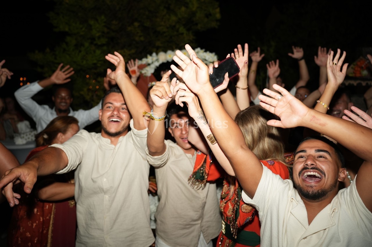 Groupe de personnes souriantes levant les bras en l'air lors d'une fête en extérieur, ambiance festive et animée.