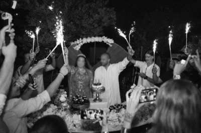 Des personnes entourent un couple célébrant avec des cierges magiques autour d'une table décorée avec un gâteau.