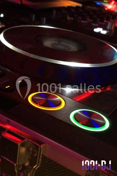 Platines DJ éclairées avec des boutons lumineux colorés et des reflets métalliques dans une ambiance sombre.
