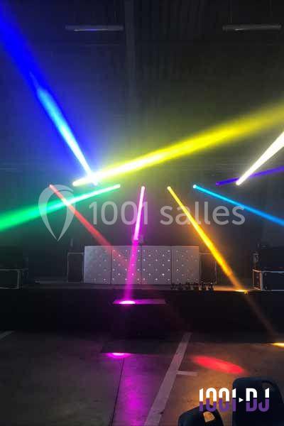 Jeu de lumières colorées projetées sur une scène sombre avec une table de DJ au centre.