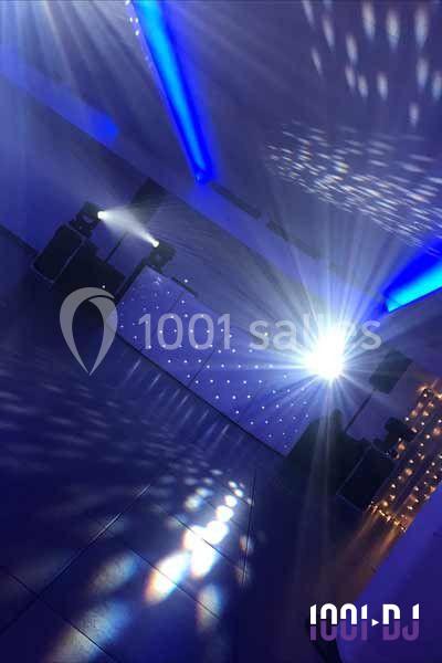 Salle de réception avec éclairage bleu, jeux de lumière et une installation DJ en arrière-plan.