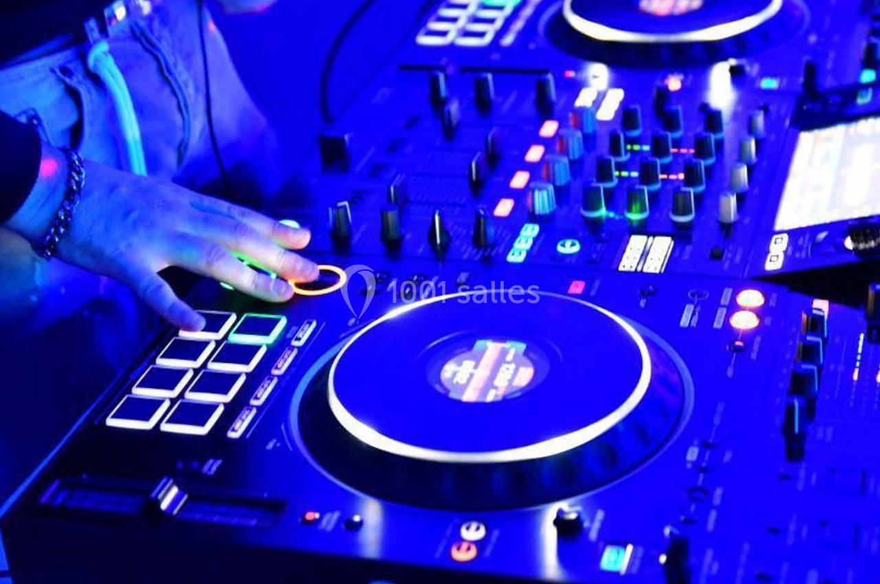 Main posée sur une table de mixage éclairée par des lumières bleues, entourée de boutons et platines.