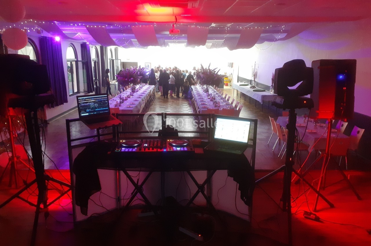 Salle de réception décorée avec des tables dressées, vue depuis une installation de DJ avec lumières colorées.