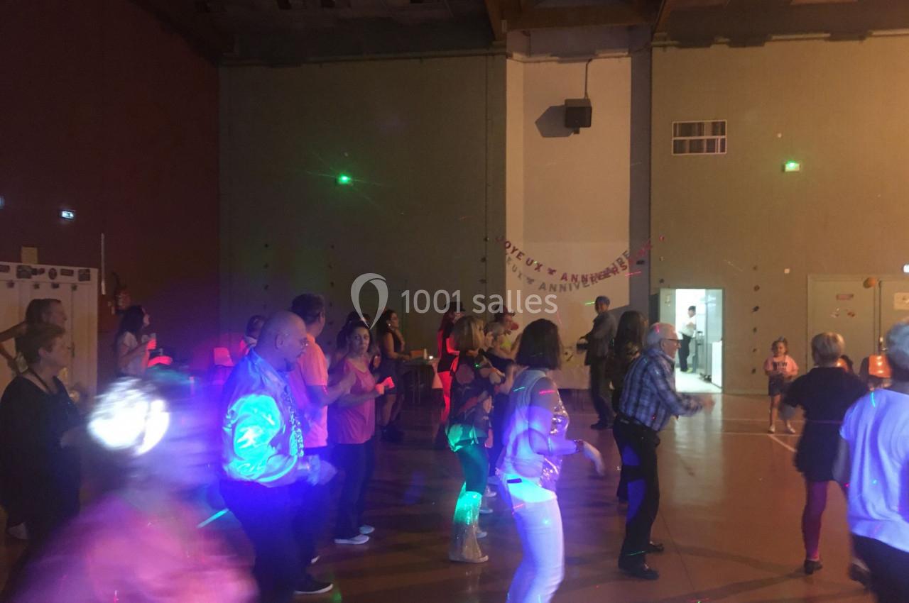 Des personnes dansent dans une salle éclairée par des lumières colorées, avec une ambiance festive en soirée.