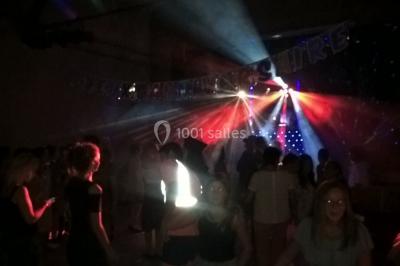 Personnes dansant sous des lumières colorées lors d'une soirée animée par un DJ dans une salle en pierre.