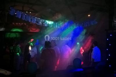 Personnes dansant sous des lumières colorées lors d'une soirée animée par un DJ dans une salle en pierre.