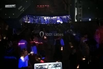 Personnes dansant sous des lumières colorées lors d'une soirée animée par un DJ dans une salle en pierre.