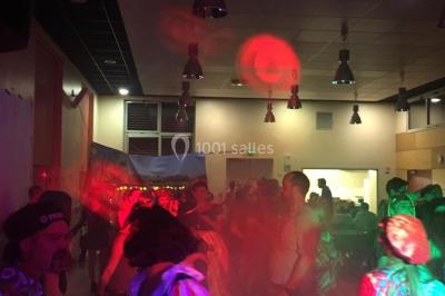Personnes dansant sous des lumières colorées lors d'une soirée animée par un DJ dans une salle en pierre.