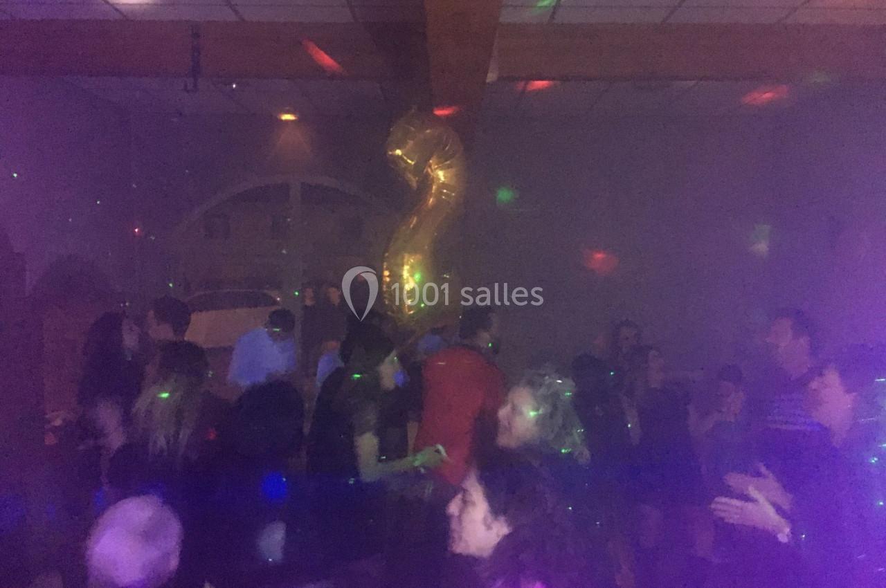 Personnes dansant dans une salle sombre avec des lumières colorées et un ballon doré en forme de chiffre 2.