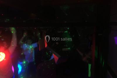 Personnes dansant sous des lumières colorées lors d'une soirée animée par un DJ dans une salle en pierre.