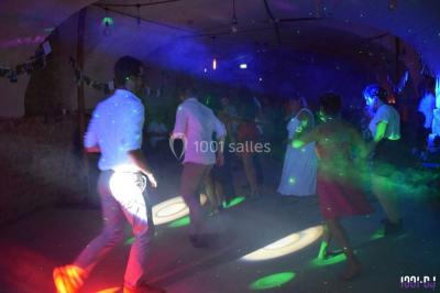 Personnes dansant sous des lumières colorées lors d'une soirée animée par un DJ dans une salle en pierre.