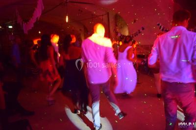 Personnes dansant sous des lumières colorées lors d'une soirée animée par un DJ dans une salle en pierre.