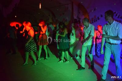 Personnes dansant sous des lumières colorées lors d'une soirée animée par un DJ dans une salle en pierre.