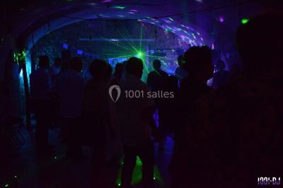 Personnes dansant sous des lumières colorées lors d'une soirée animée par un DJ dans une salle en pierre.
