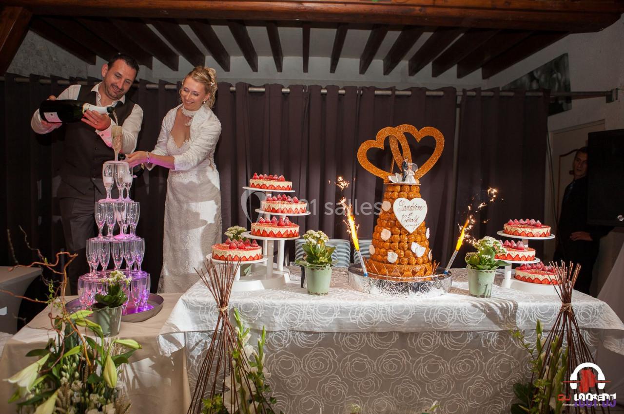 Un couple de mariés sert du champagne près d'une table décorée avec des desserts et une pièce montée.