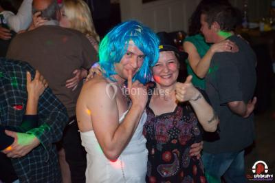 Des personnes dansent en ligne dans une salle décorée de ballons, avec des tables dressées et des convives en arrière-plan.