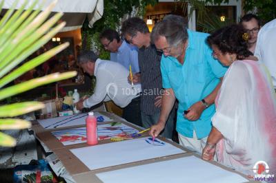 Des personnes dansent en ligne dans une salle décorée de ballons, avec des tables dressées et des convives en arrière-plan.