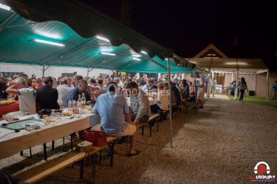 Des personnes dansent en ligne dans une salle décorée de ballons, avec des tables dressées et des convives en arrière-plan.