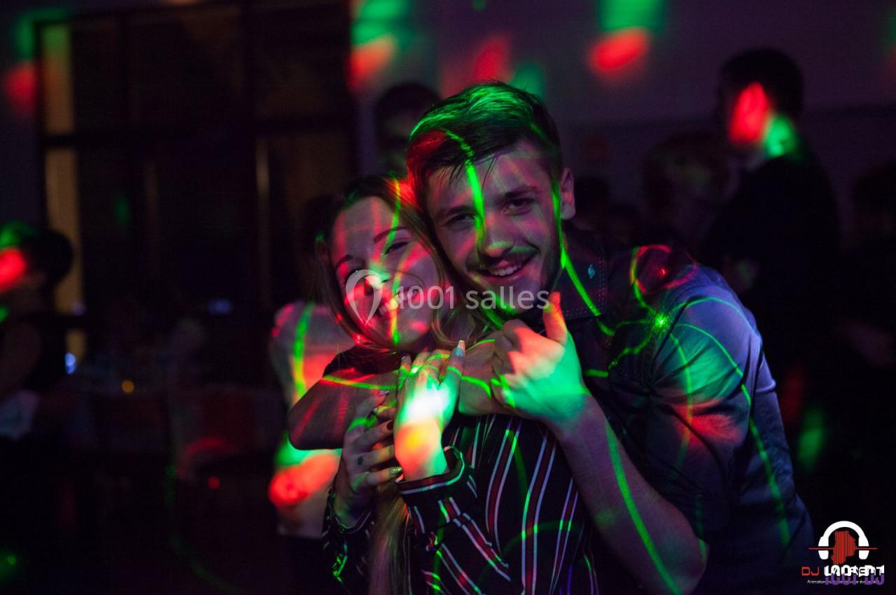 Un homme et une femme sourient et posent ensemble dans une ambiance festive avec des lumières colorées.